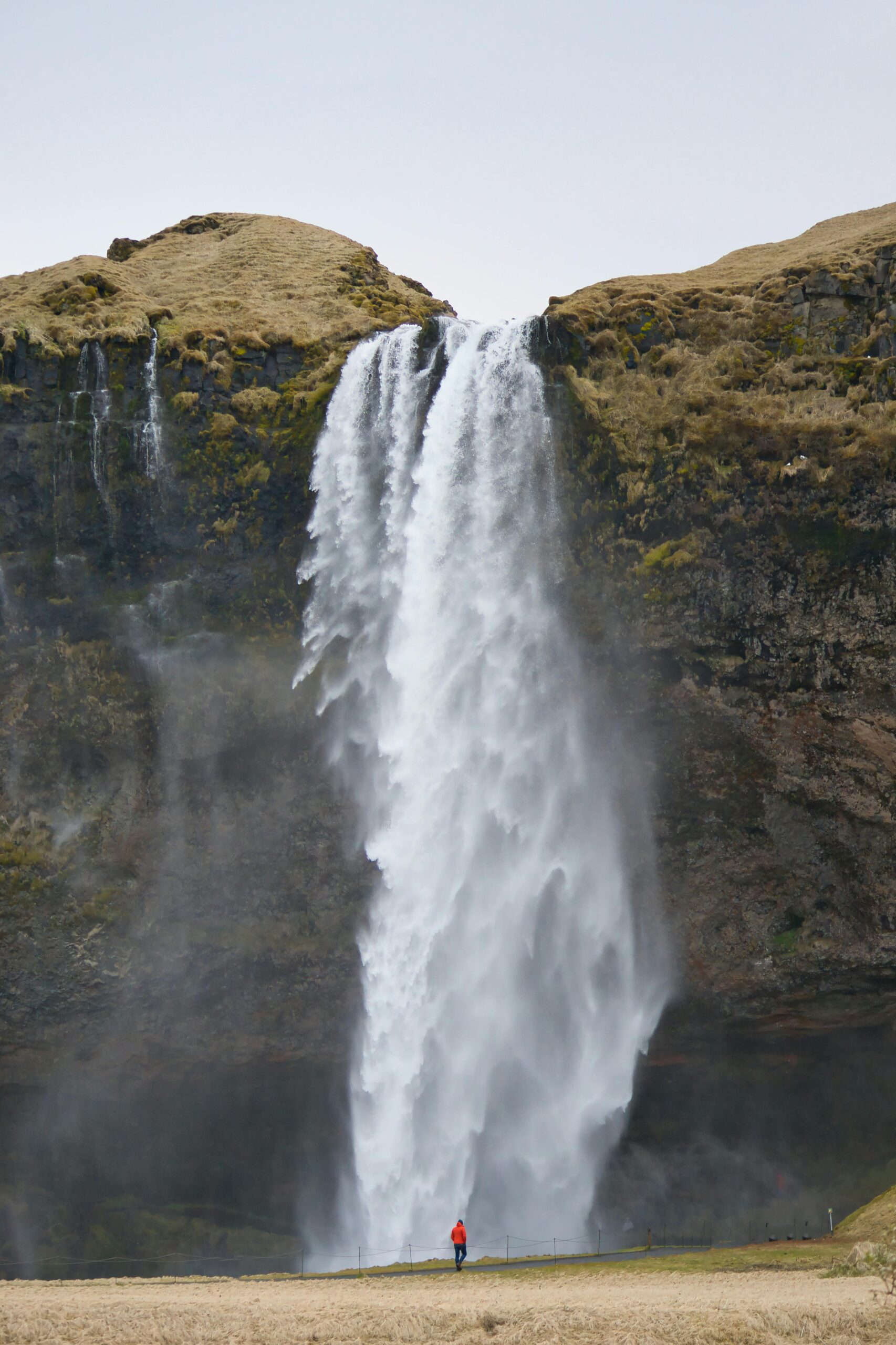 Stunning waterfall cascades down cliffs in Islandia, a small figure adds scale.